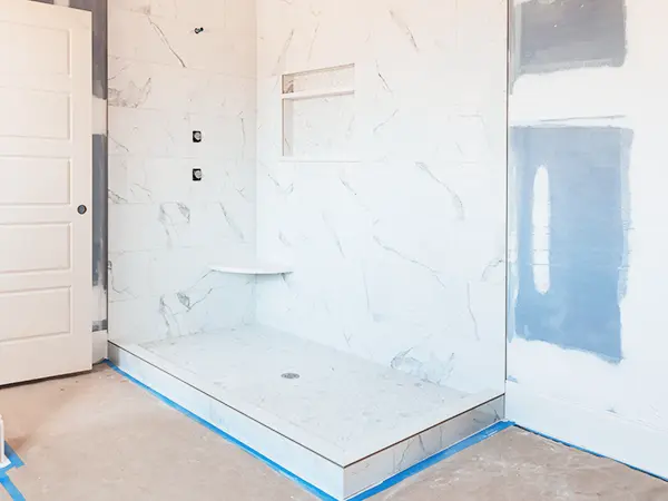 In-progress tub-to-shower conversion featuring marble-style walls and built-in shelf for a sleek, modern look