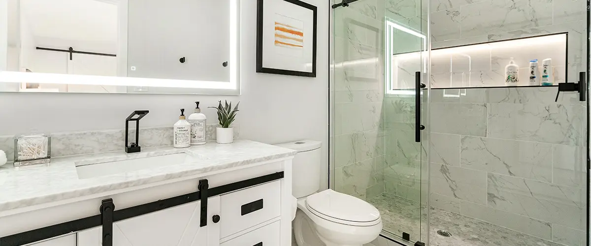 Modern bathroom renovation with illuminated mirror, white vanity, and sleek glass-enclosed shower in marble tile design.