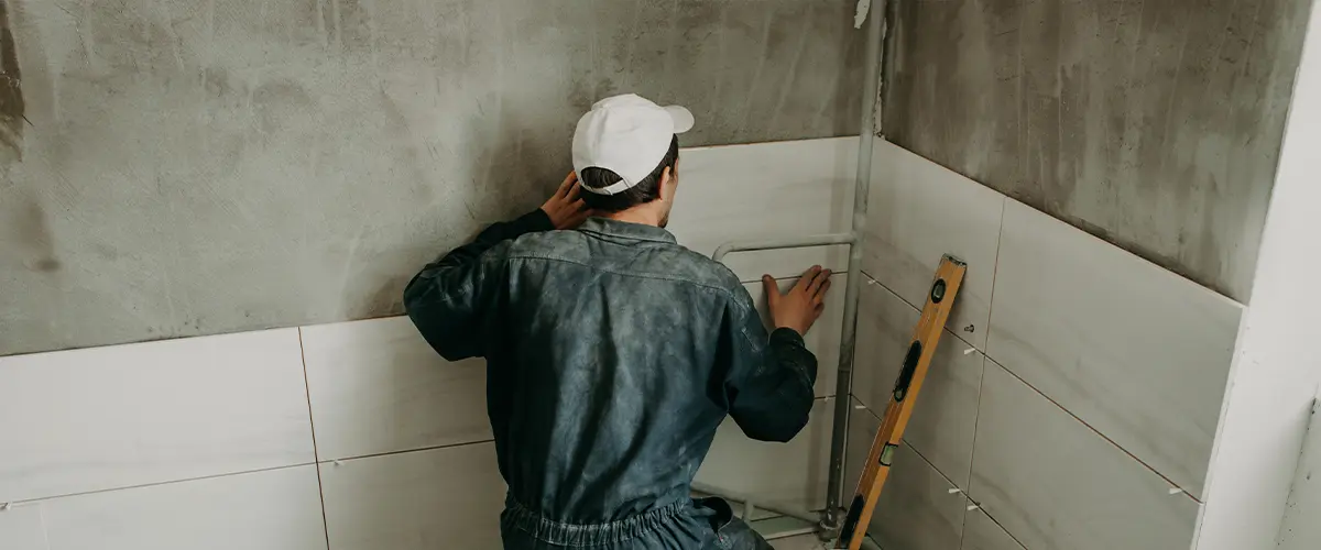 Worker installing white ceramic tiles on bathroom walls, renovation and construction project.