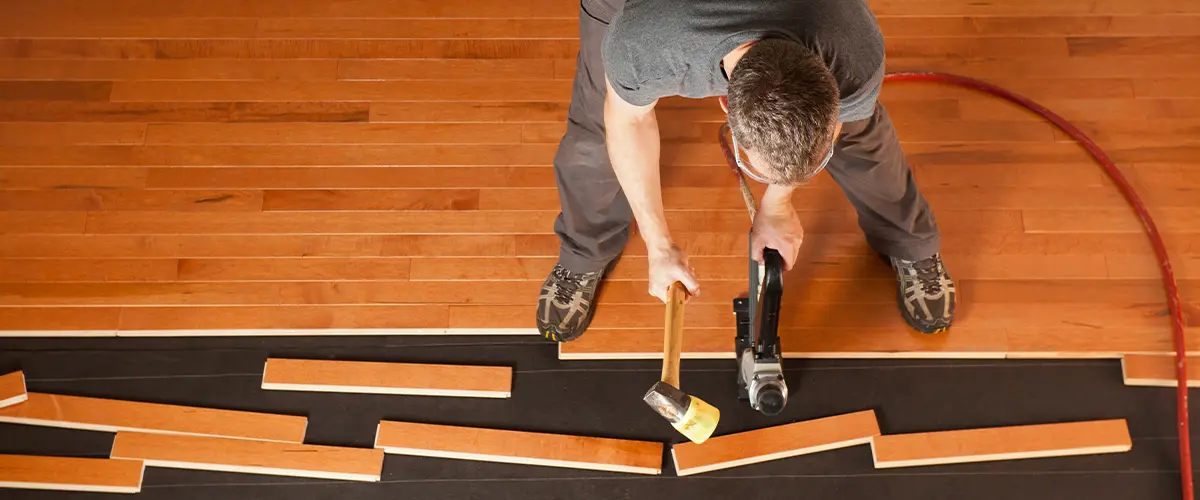 Hardwood flooring installation with contractor using a mallet and nailer